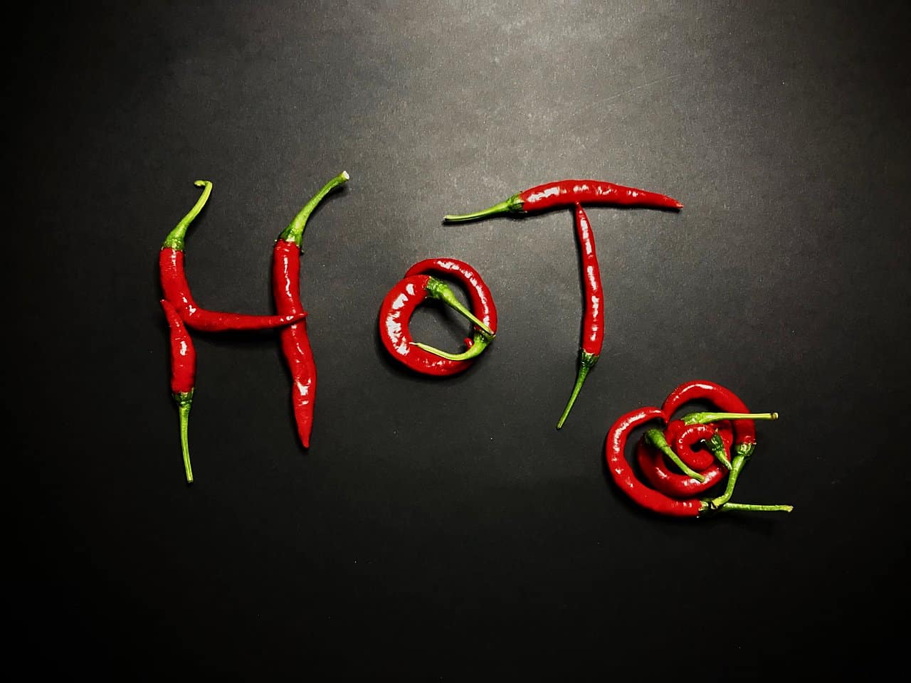 Nápis HOT vyskladaný z čerstvých chilli papričiek na čiernom pozadí