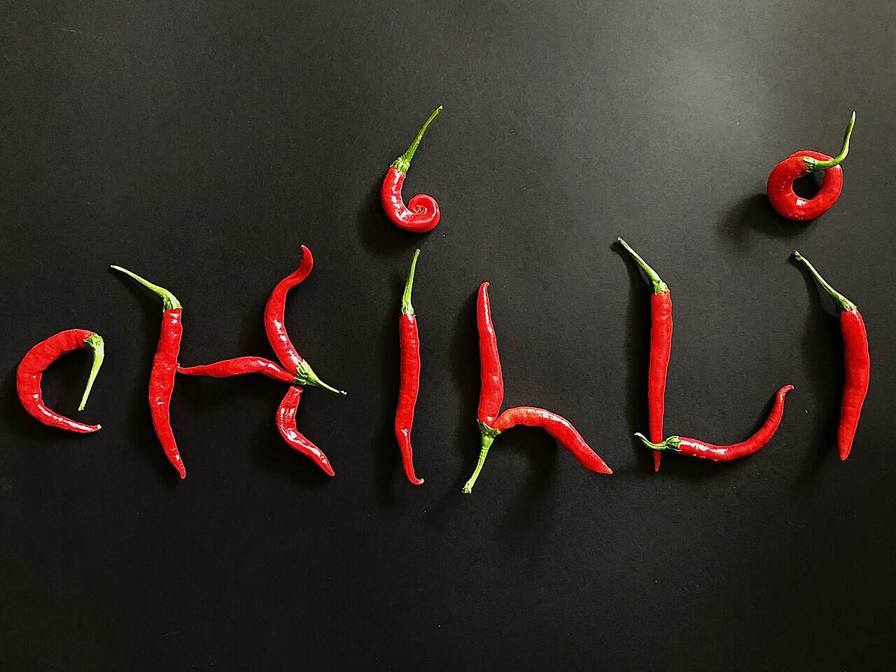 Nápis chilli vyskladaný z čerstvých papričiek na čiernom pozadí