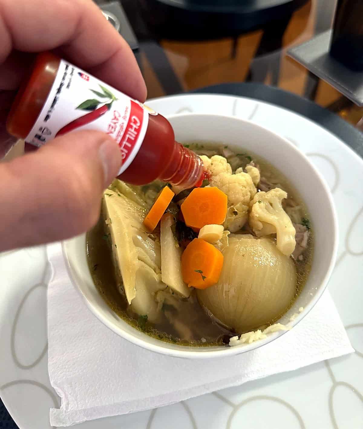 Dávkovanie tekutého chilli Cayenne po kvapkách do slepačieho vývaru